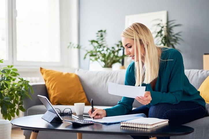 Young woman sitting on a couch and coffee table working on business taxes and analytics.