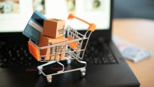 A tiny grocery cart filled with small boxes and a debit card resting on top of a laptop.